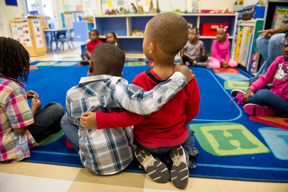 two toddlers hugging, from behind, in a colorful classroom