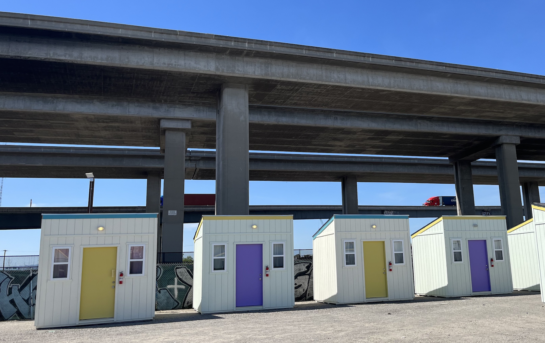 four colorful cabins in front of elevated highway with a blue sky