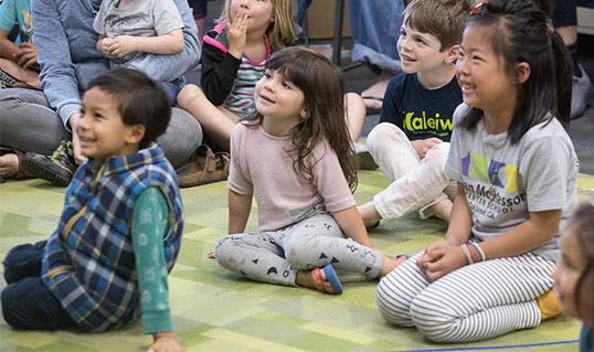 Young children sitting on a carpet during a magic show at OPL.