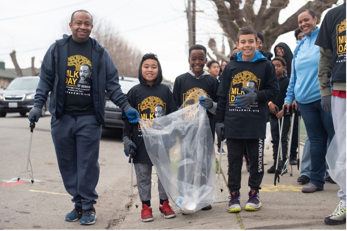 group of five people in matching black sweatshirts holding a trash bag