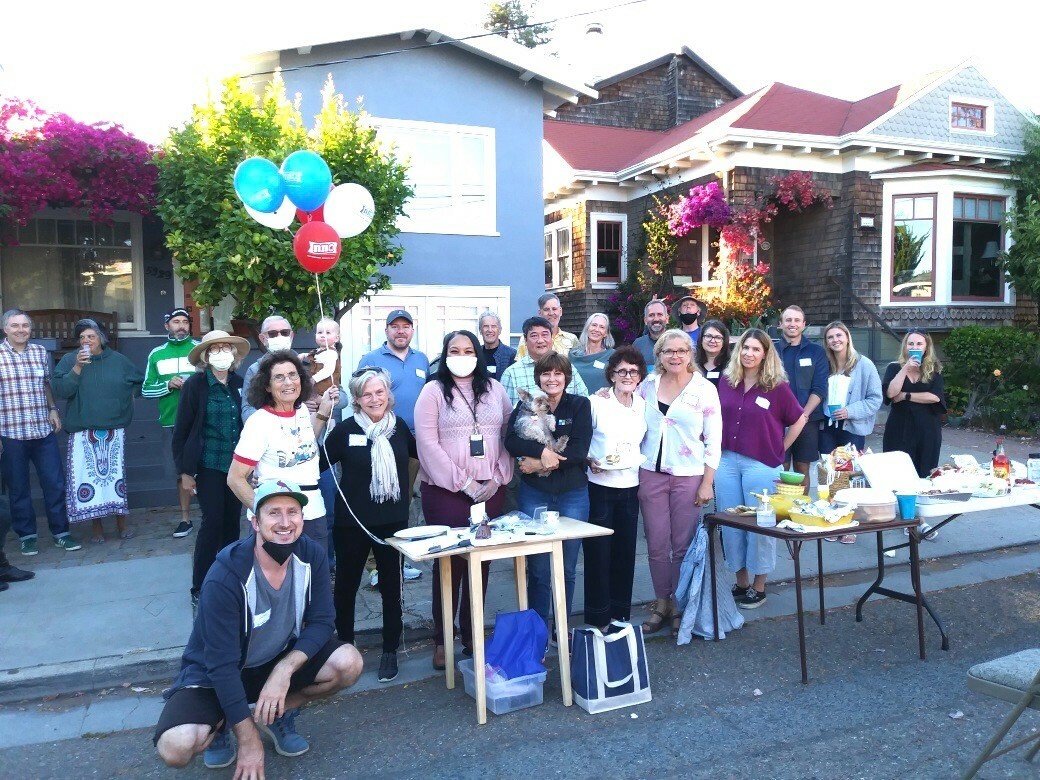 group of neighbors standing at tables in the street in front of houses with balloons