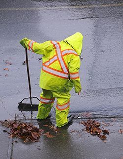 Photo of a person cleaning a storm drain in the rain